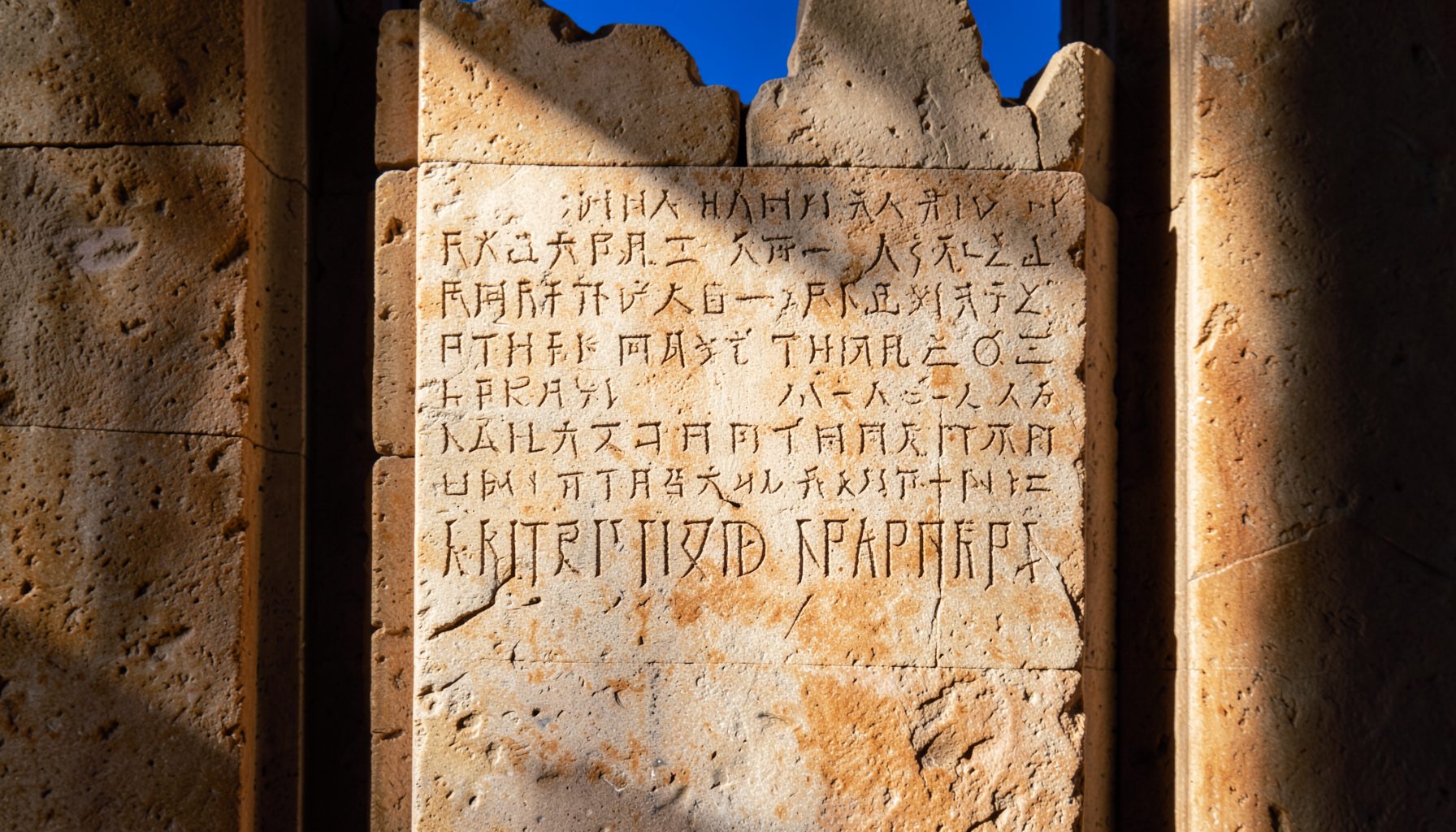 Warm-toned close-up of an ancient textured stone tablet with carved inscriptions, soft natural light raking across the surface, earthy beige and ochre tones