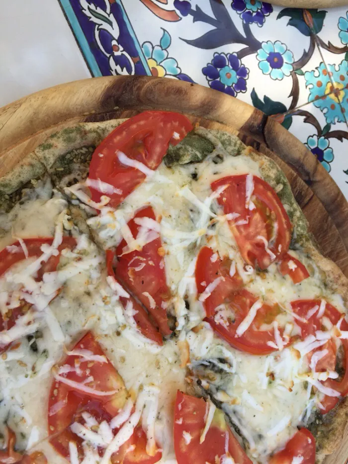 Overhead view of a rustic flatbread topped with tomato and cheese on a wooden board, warm Mediterranean tones